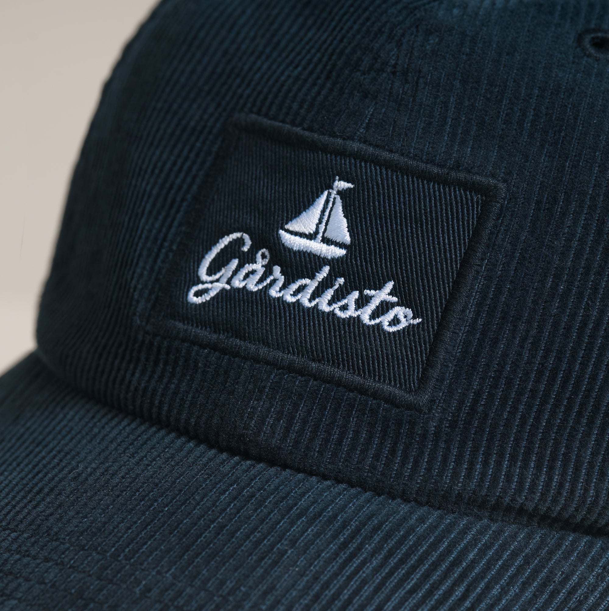 Brodert Gårdisto-logo med seilbåt på marineblå cordfløyelscaps